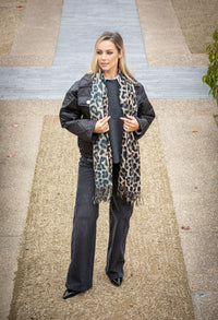 Person wearing a black jacket, scarf, and jeans on a sidewalk.