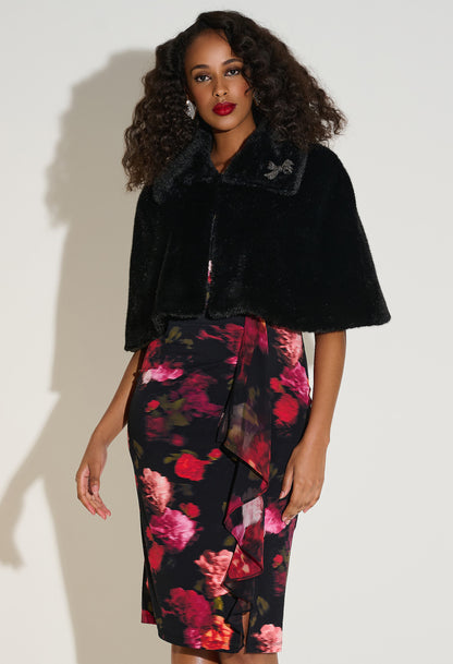 Woman wearing a black cape over a floral dress against a white background