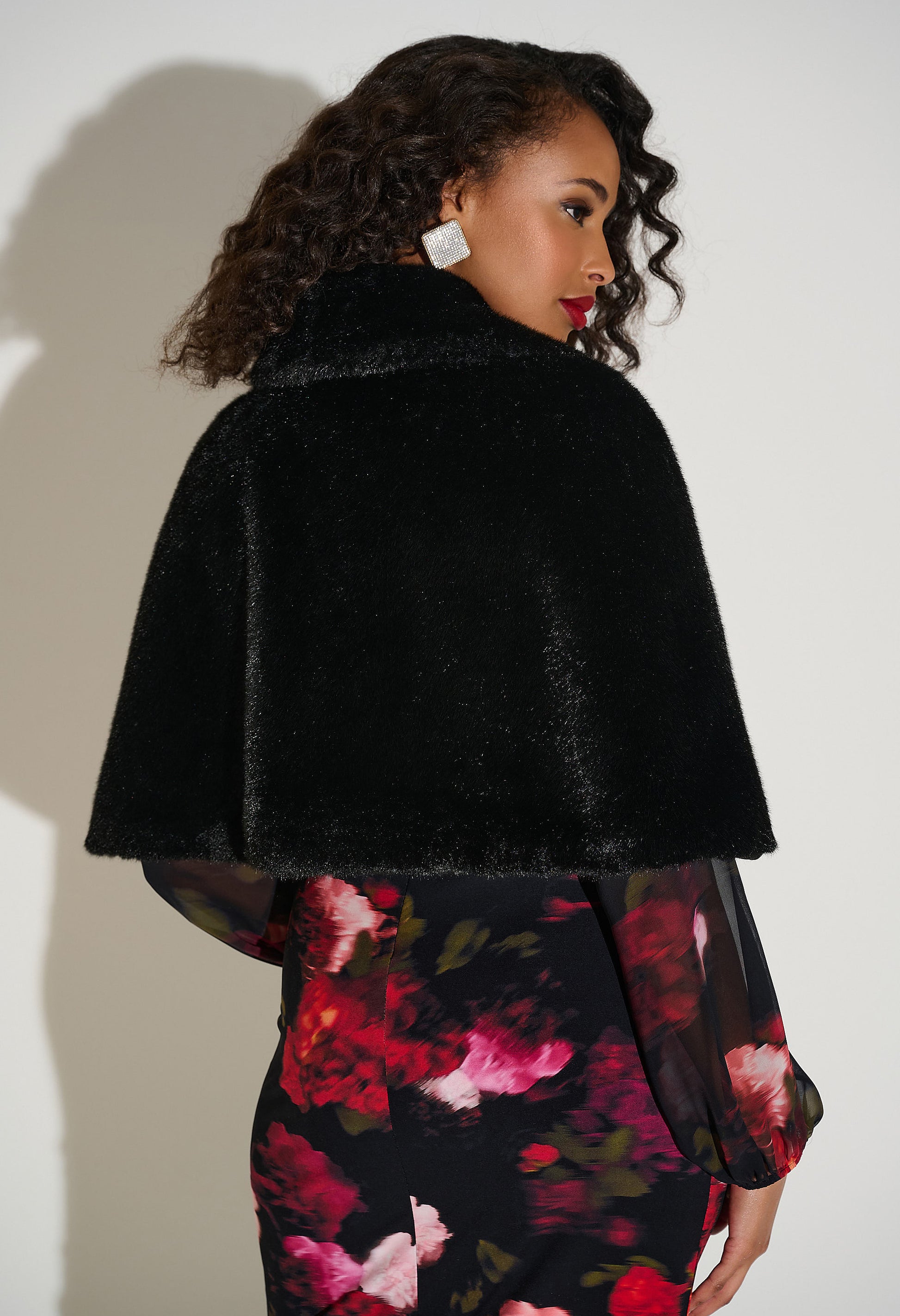 Woman wearing a black fur Capelet over a floral dress against a white background
