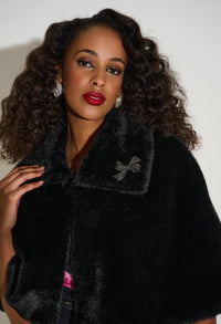 Woman wearing a black fur coat with a bow detail on a plain background