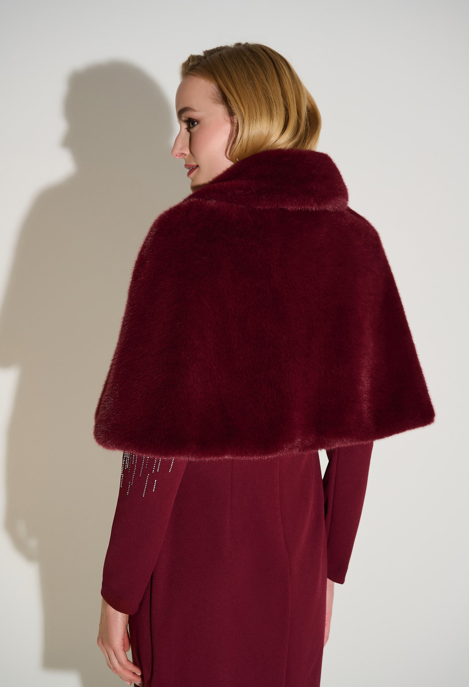 Woman wearing a burgundy fur cape against a white background