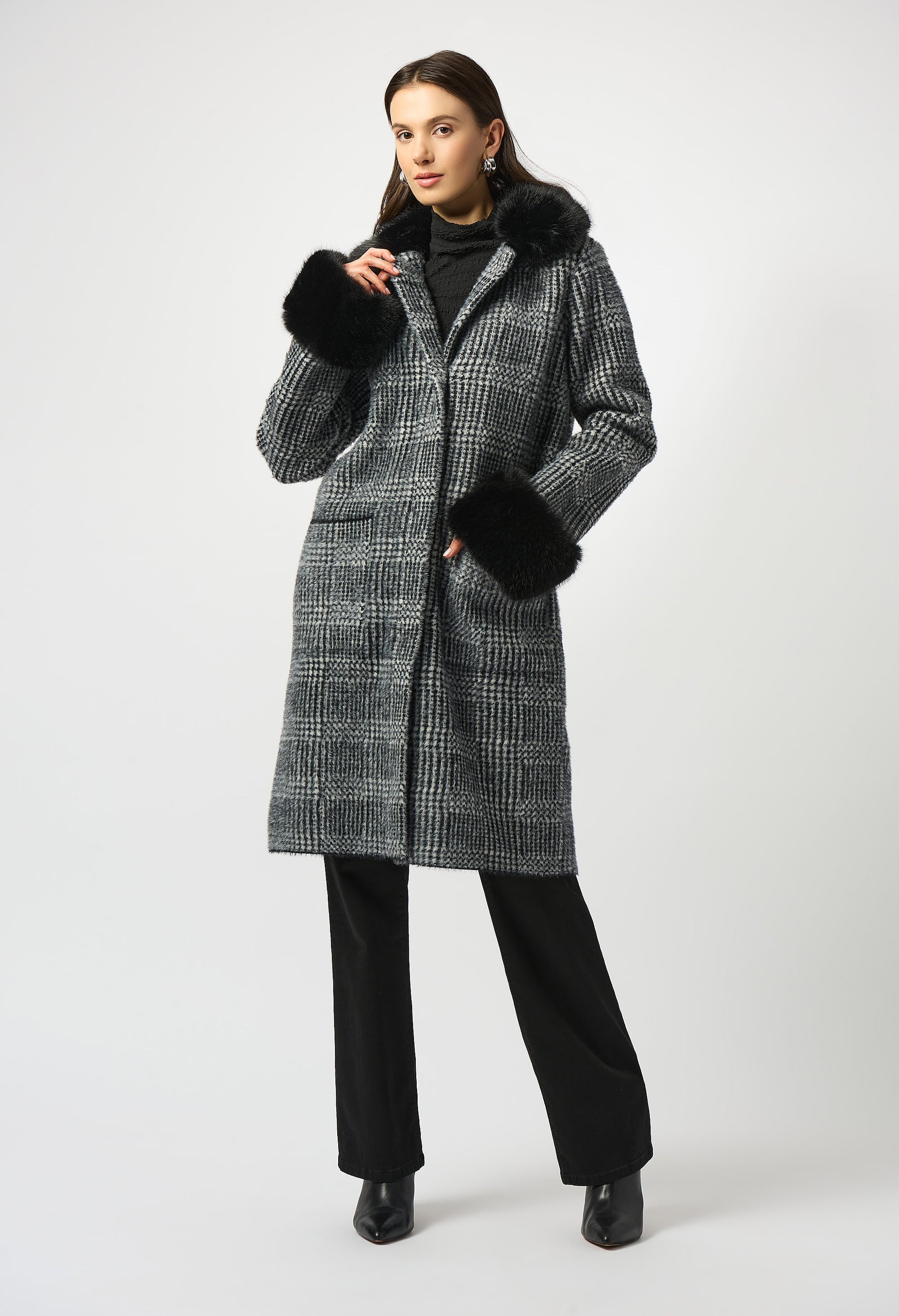 Woman wearing a long checkered coat with fur-lined hood on a white background