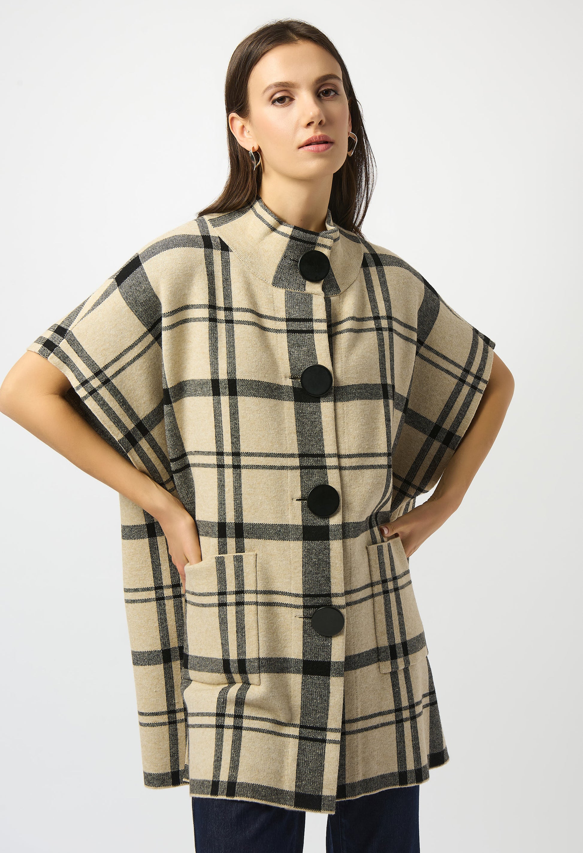 Woman wearing a plaid poncho with black buttons on a white background