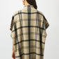 Person wearing a beige and black plaid poncho on a white background
