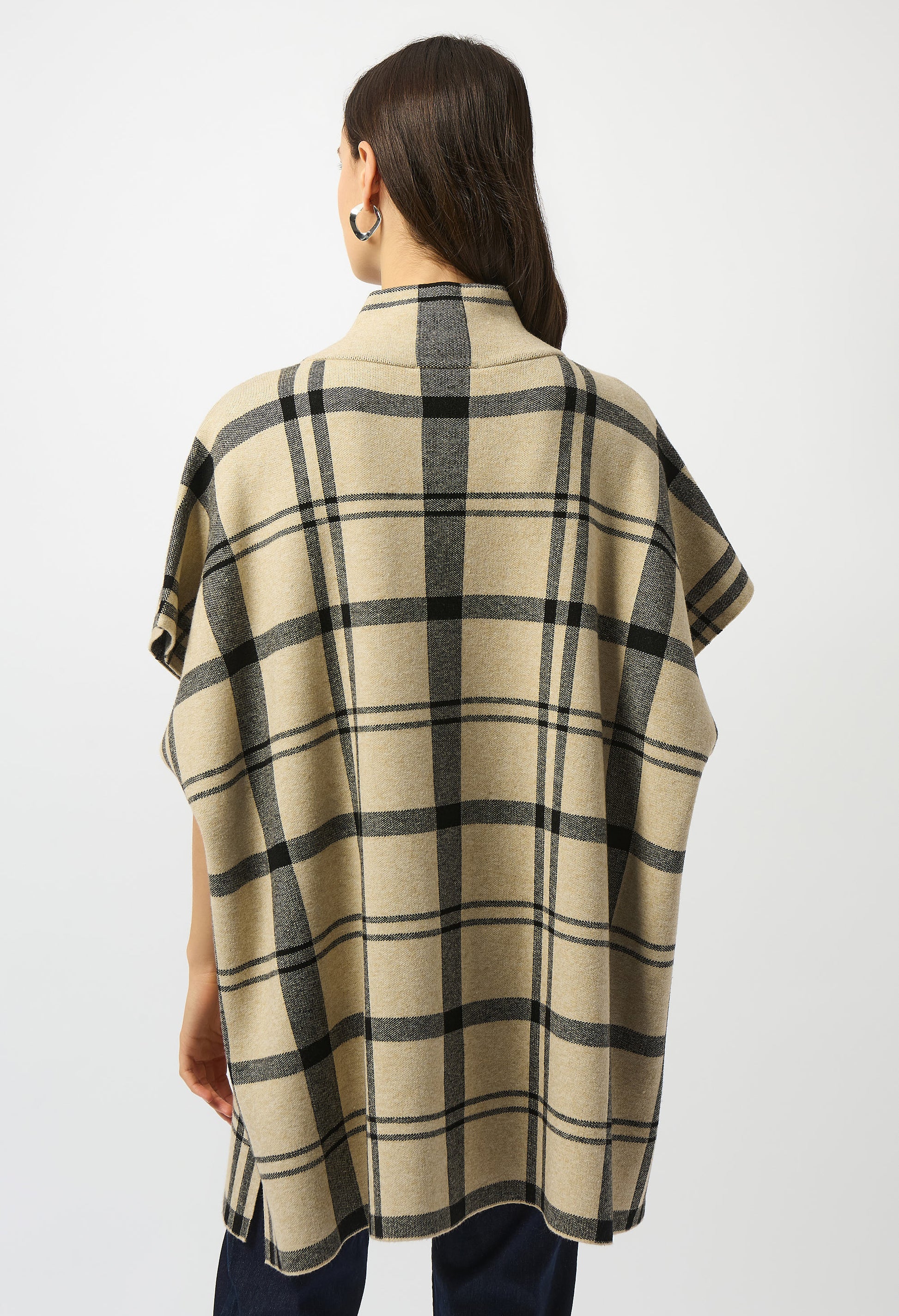 Person wearing a beige and black plaid poncho on a white background