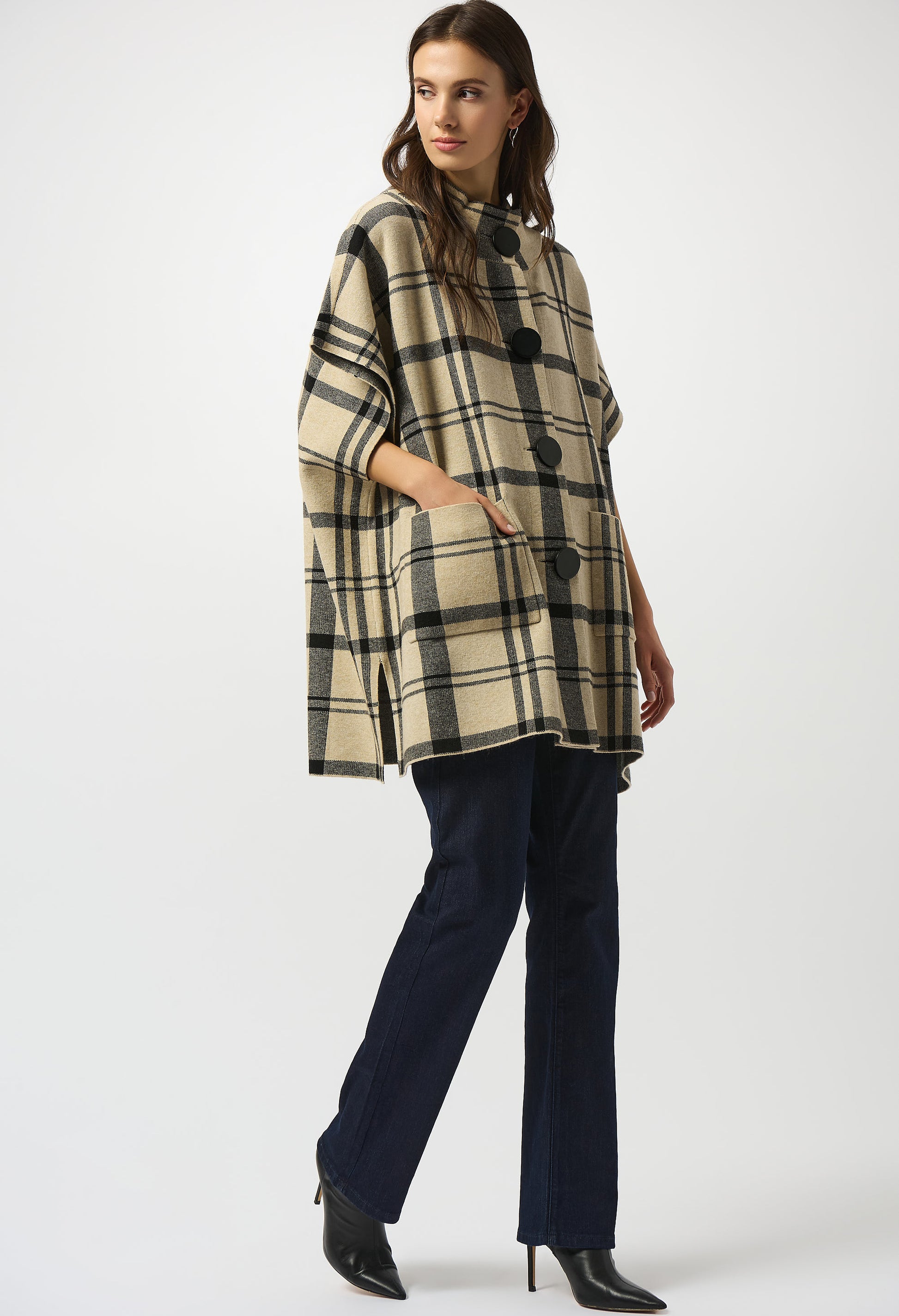 Woman wearing a plaid poncho over a dark outfit on a white background