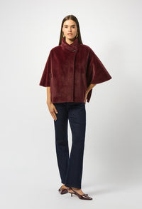 Woman wearing a burgundy cape over a black top and pants on a white background