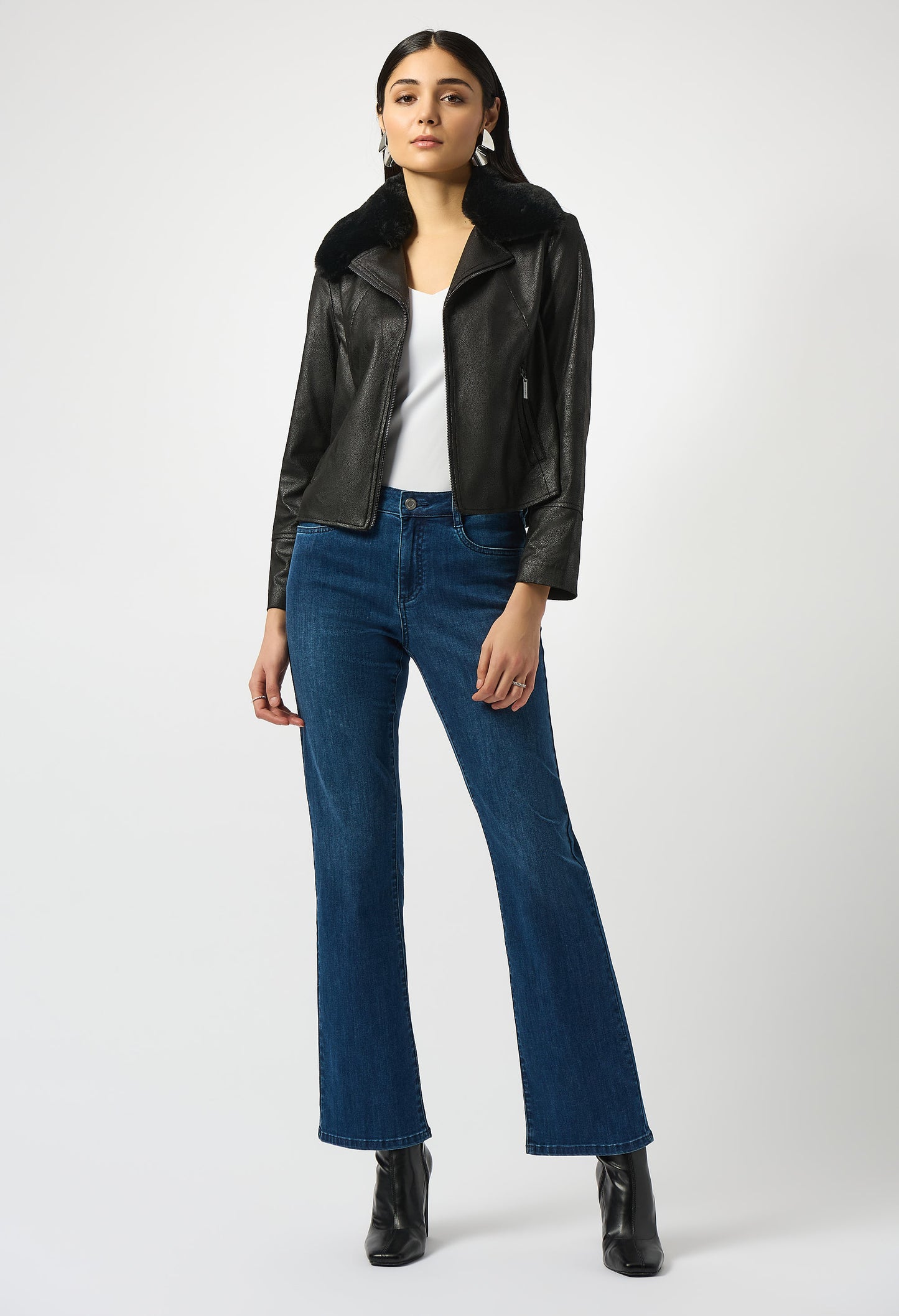 Woman wearing a black leather jacket, white top, blue jeans, and black boots on a white background