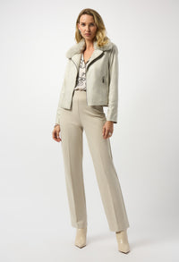Woman wearing a light gray jacket with fur collar, patterned blouse, and beige pants on a white background