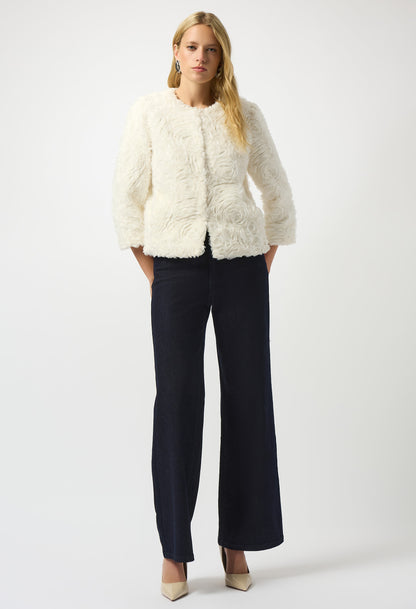 Woman wearing a white fluffy jacket and dark pants on a white background