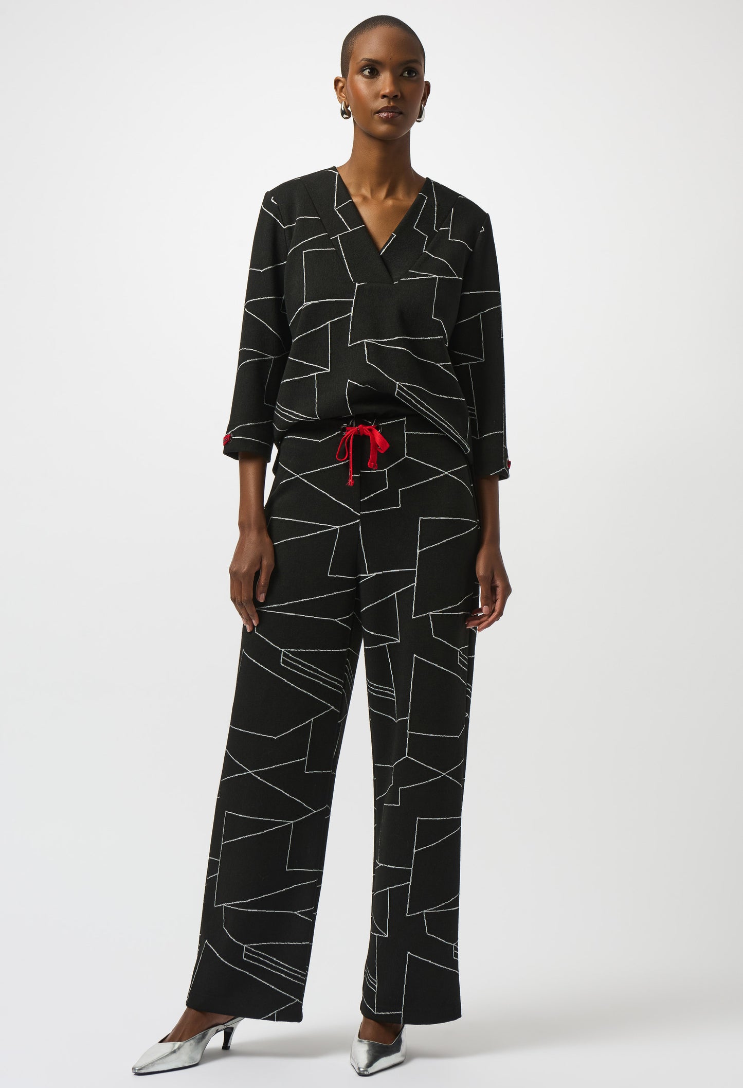 Woman wearing a black geometric patterned outfit with a red belt on a white background