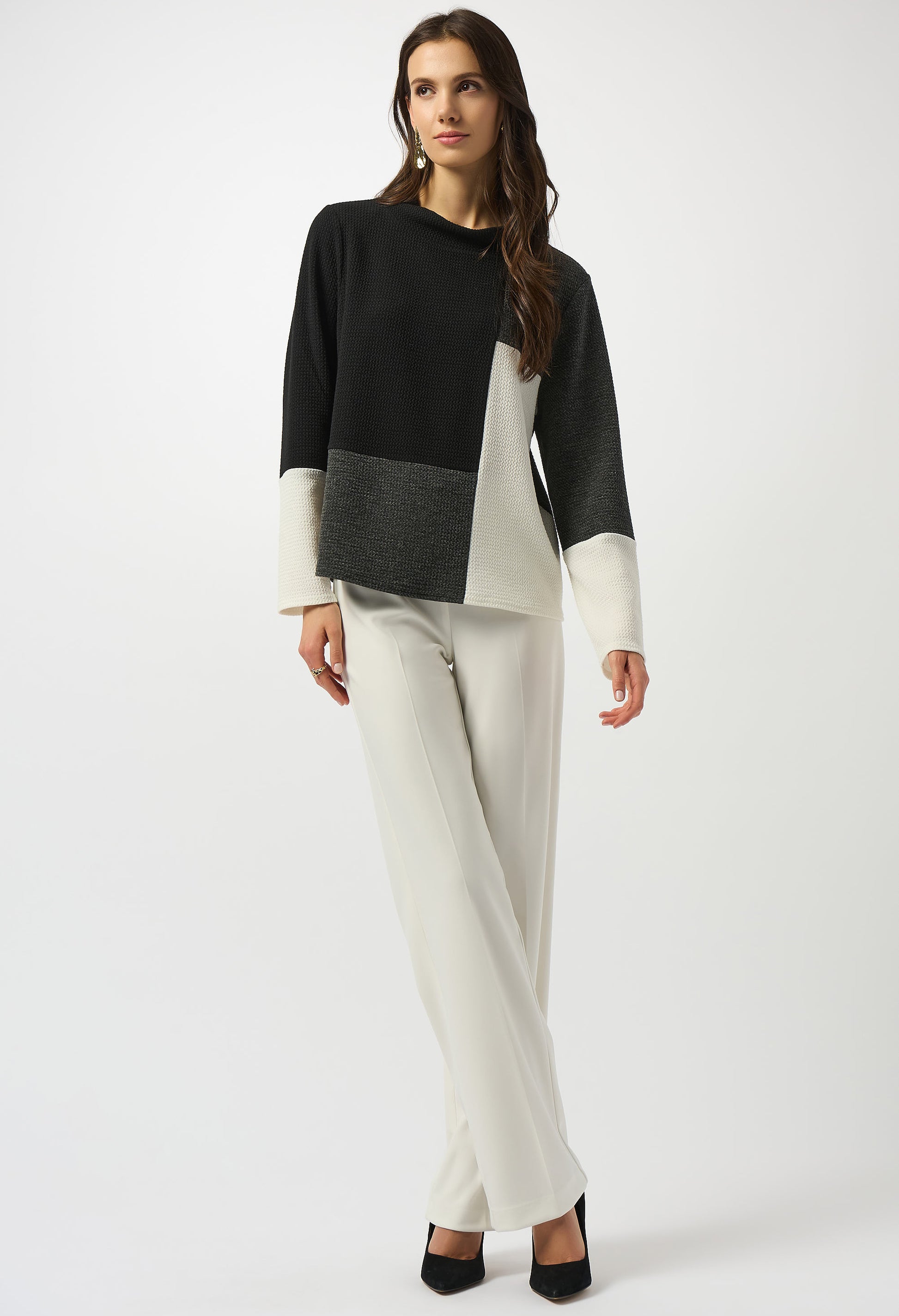 Woman wearing a black, gray, and white color-blocked sweater with white pants on a white background