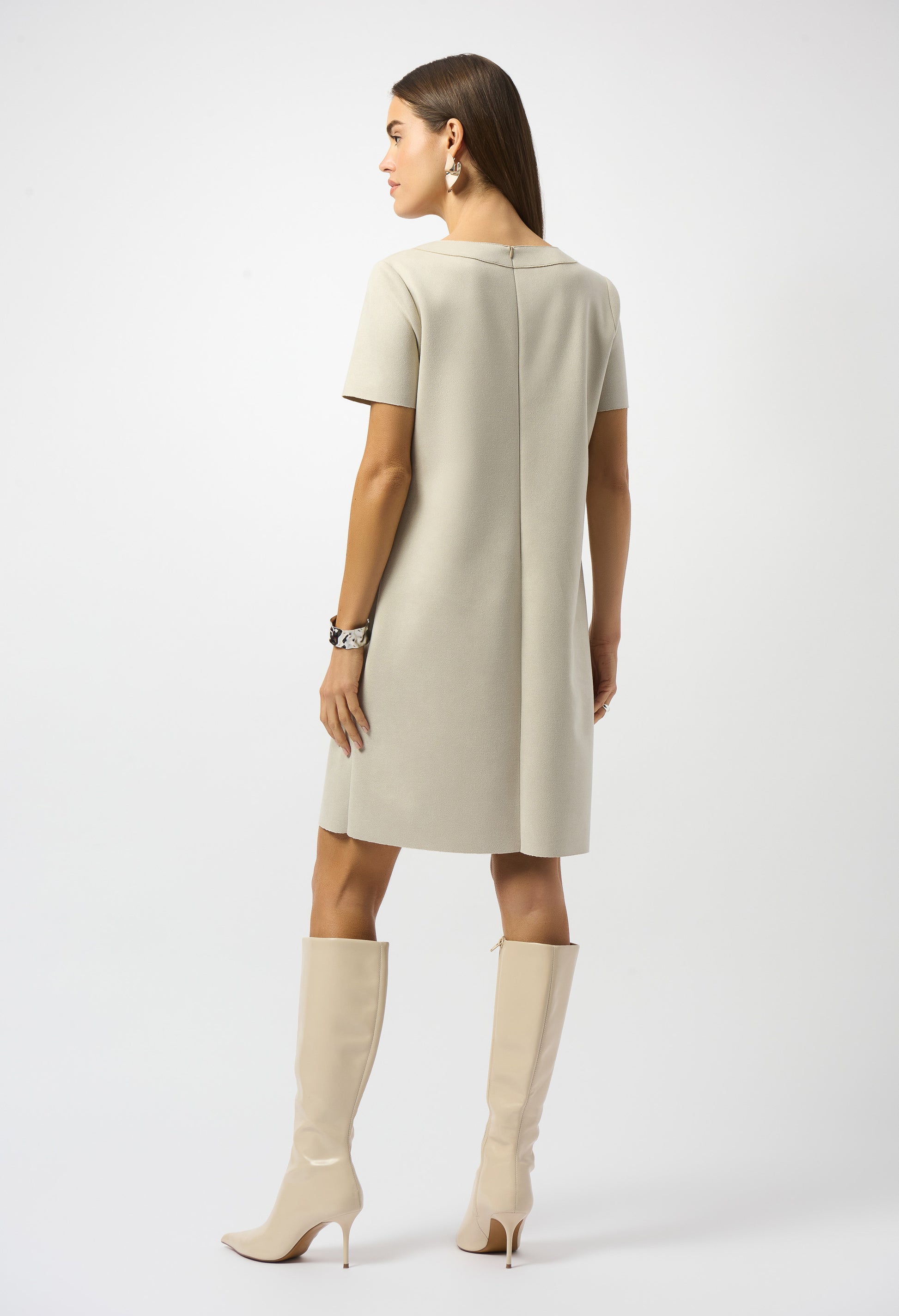 Woman wearing a beige dress and knee-high boots on a white background