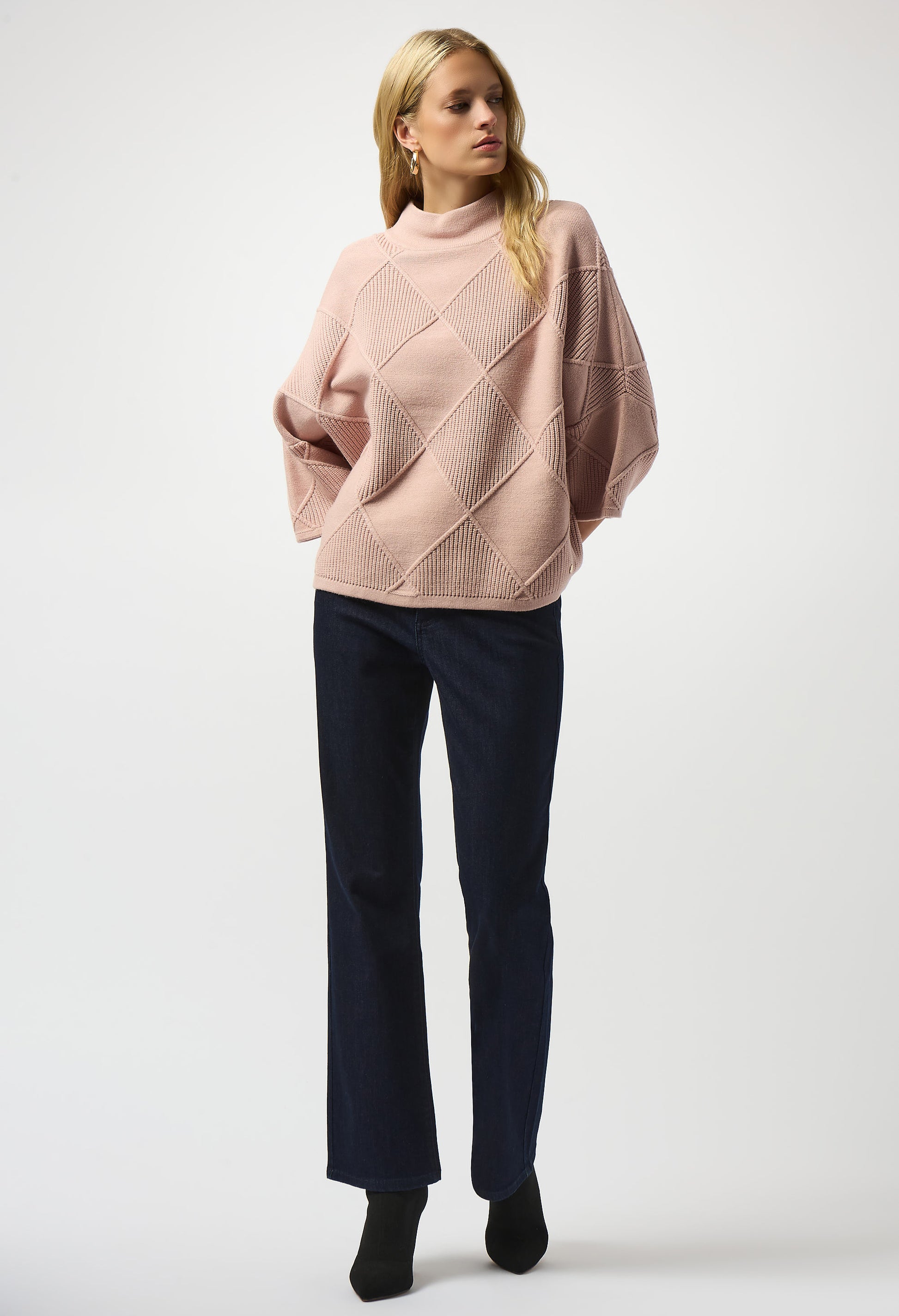 Woman wearing a pink sweater and dark pants on a white background