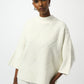 Woman wearing a white knit poncho against a plain background