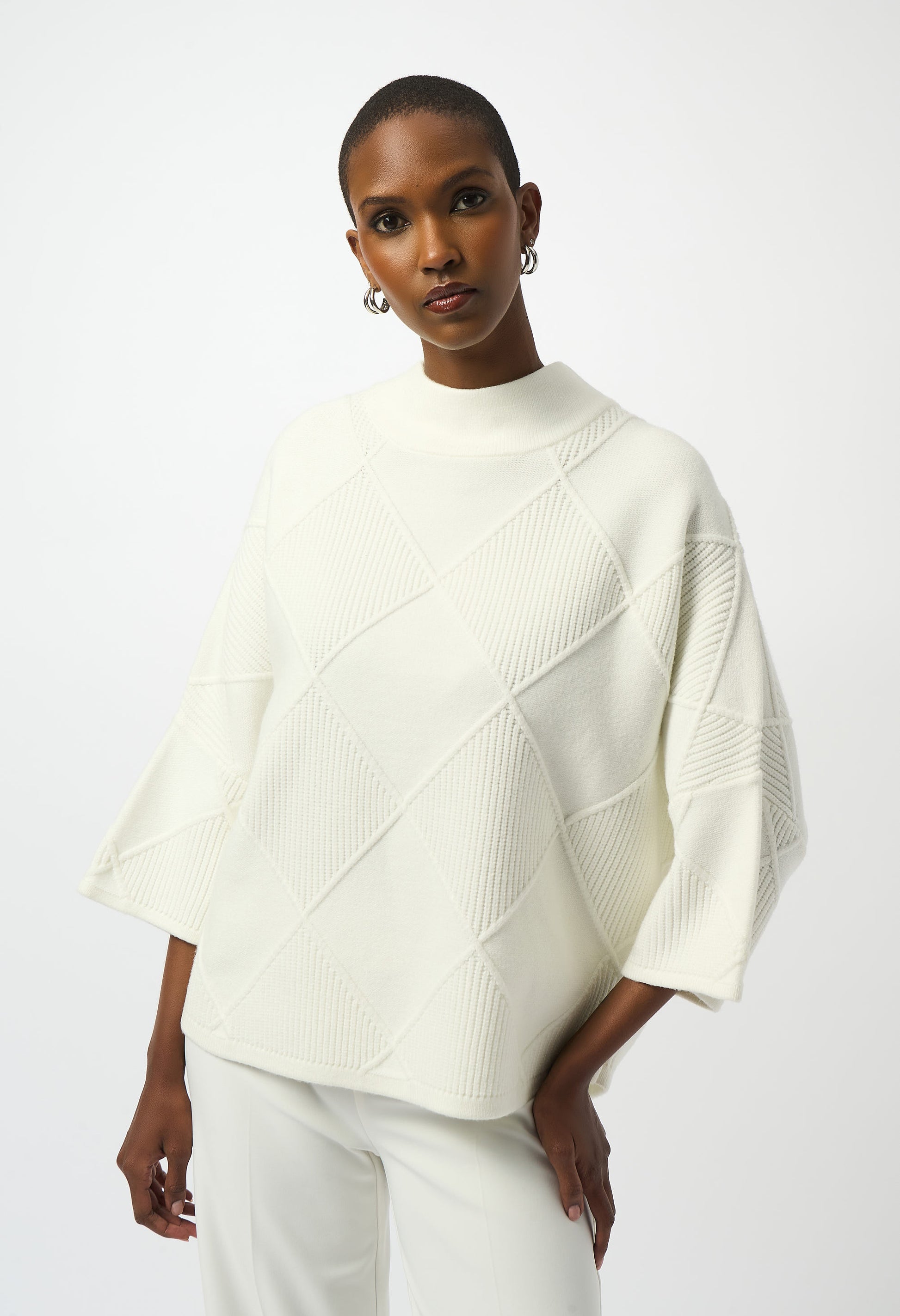 Woman wearing a white knit poncho against a plain background