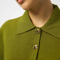 Close-up of a person wearing a green coat with gold buttons on a neutral background