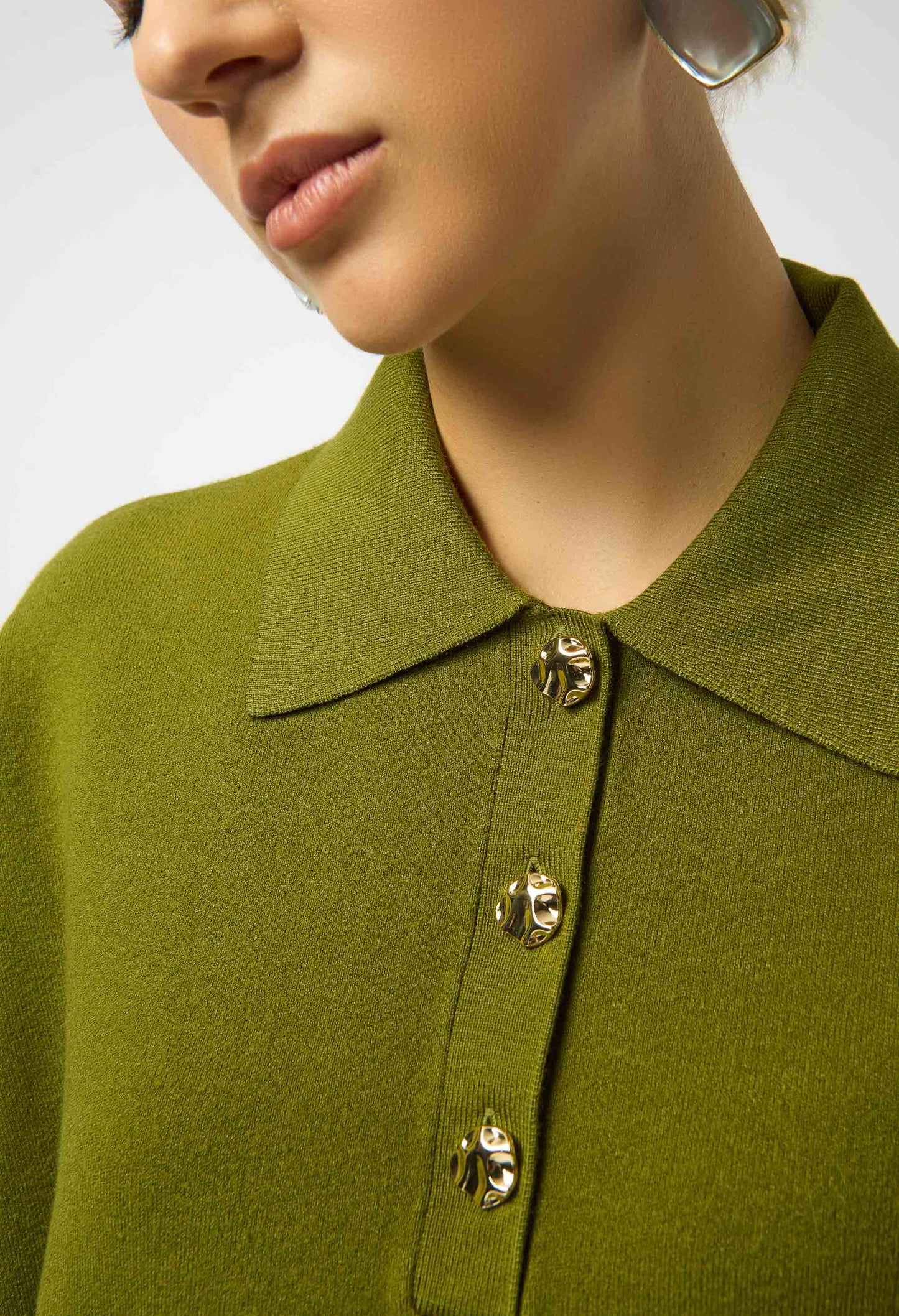 Close-up of a person wearing a green coat with gold buttons on a neutral background