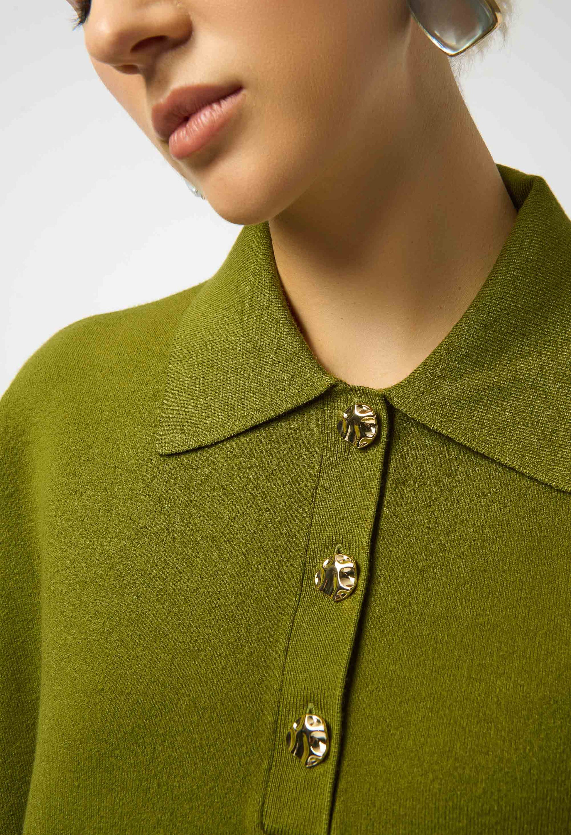 Close-up of a person wearing a green coat with gold buttons on a neutral background