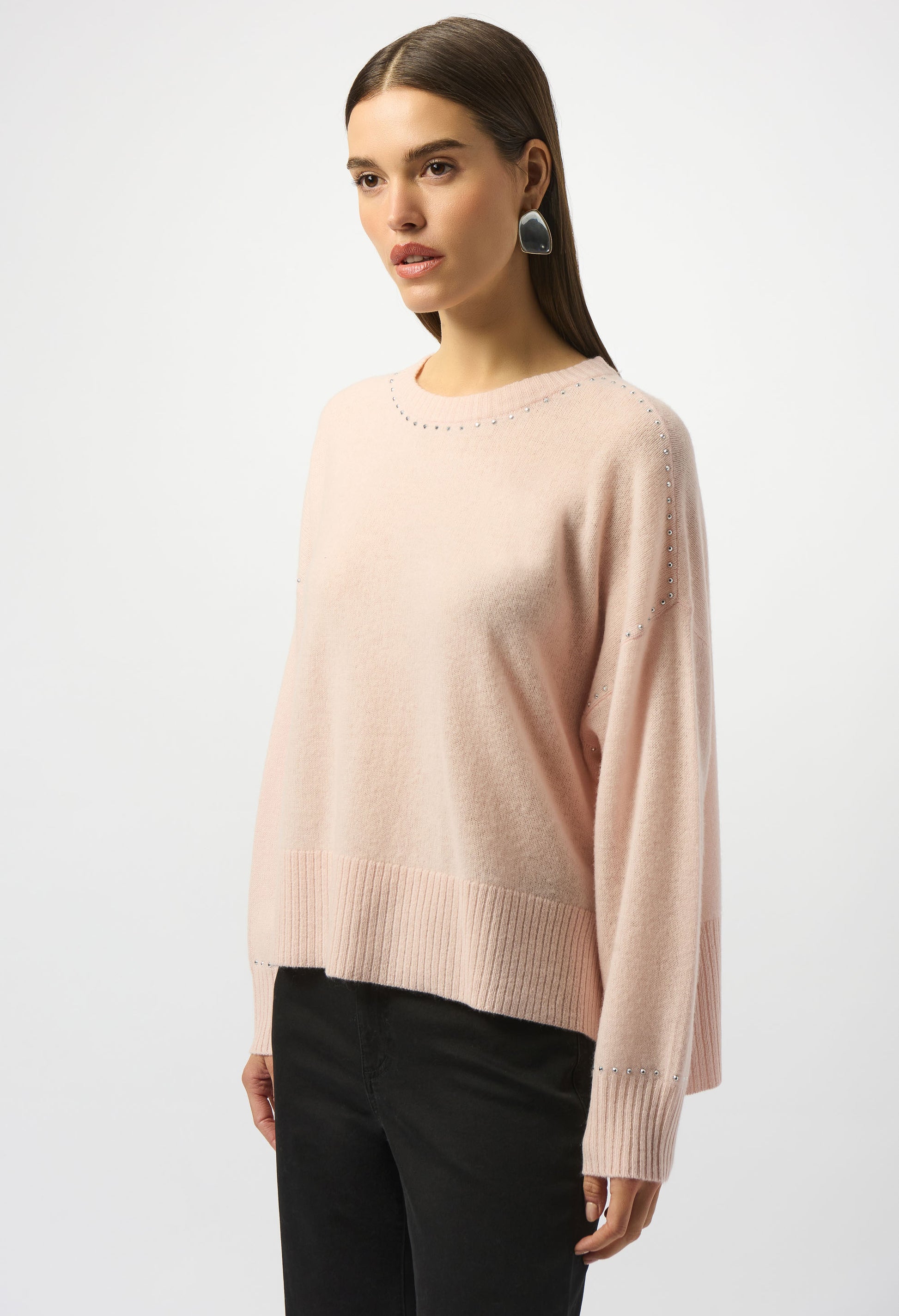 Woman wearing a light pink sweater and black pants on a white background