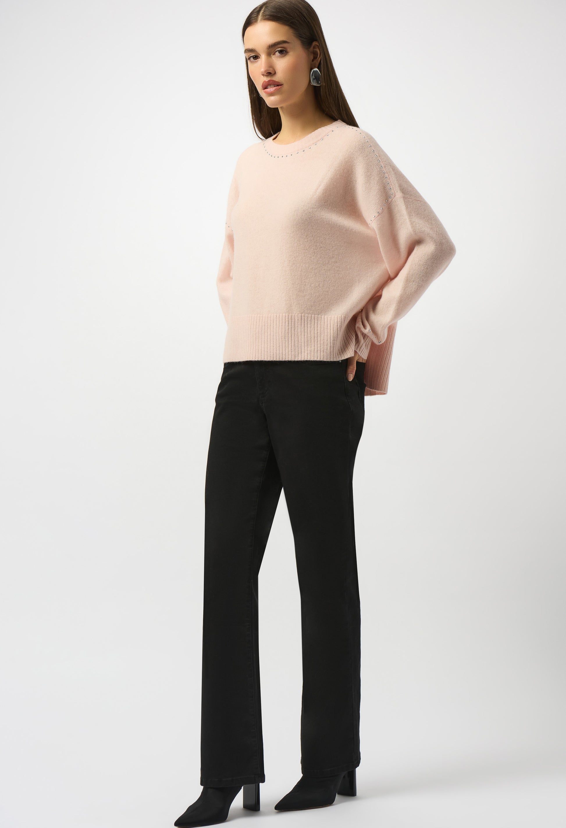 Woman wearing a light pink sweater and black pants on a white background