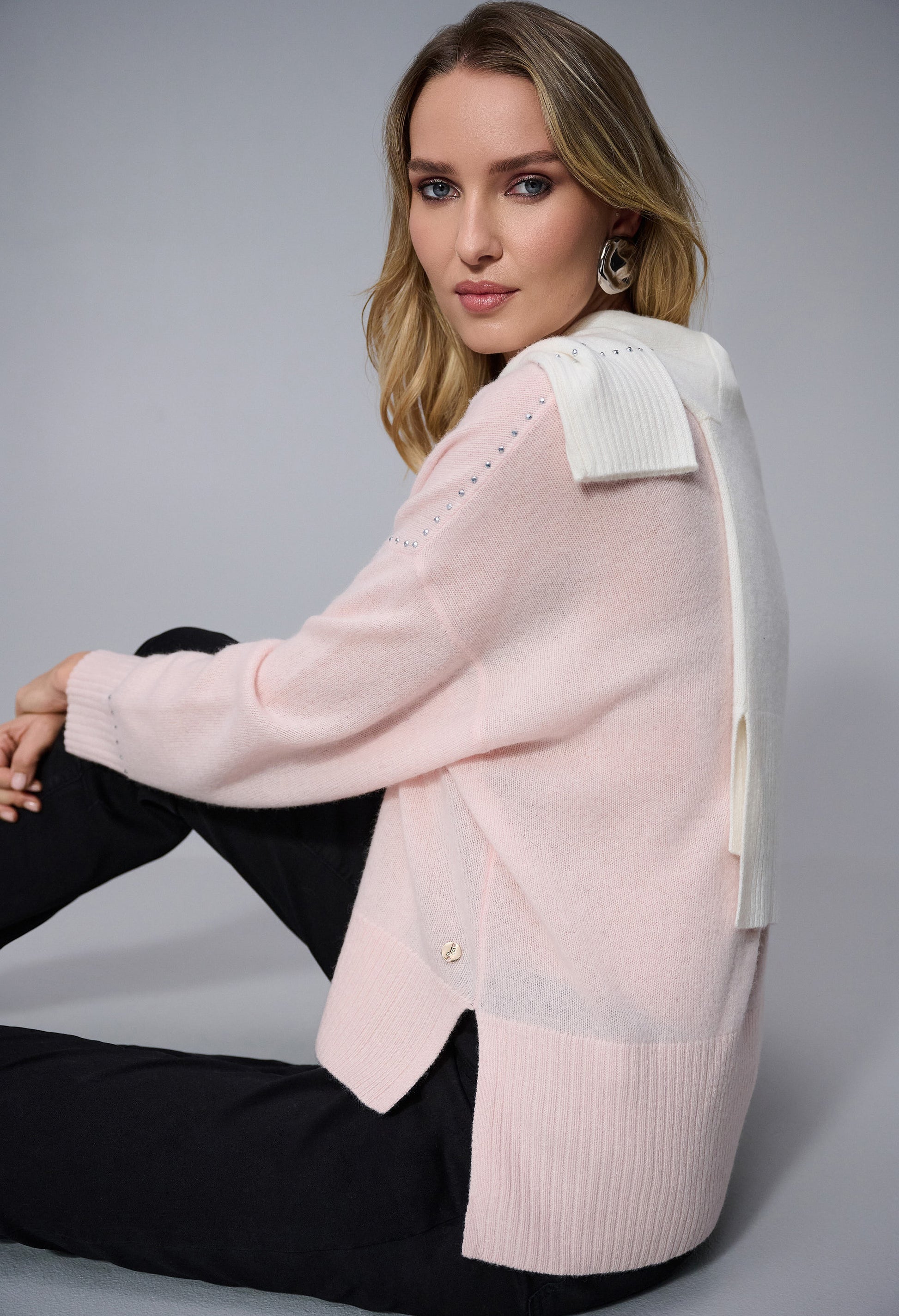 Woman wearing a pink cardigan with a white collar against a gray background