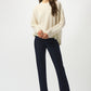 Woman wearing a cream sweater and navy pants on a white background