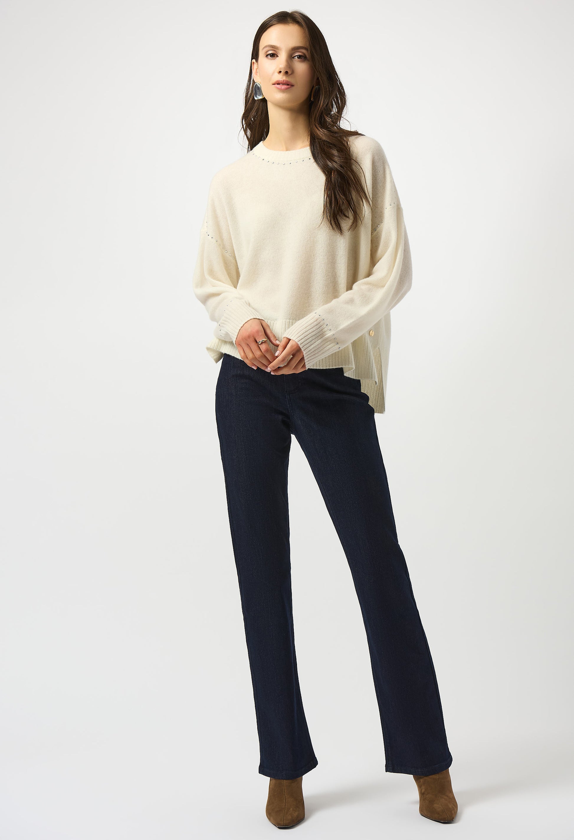 Woman wearing a cream sweater and navy pants on a white background