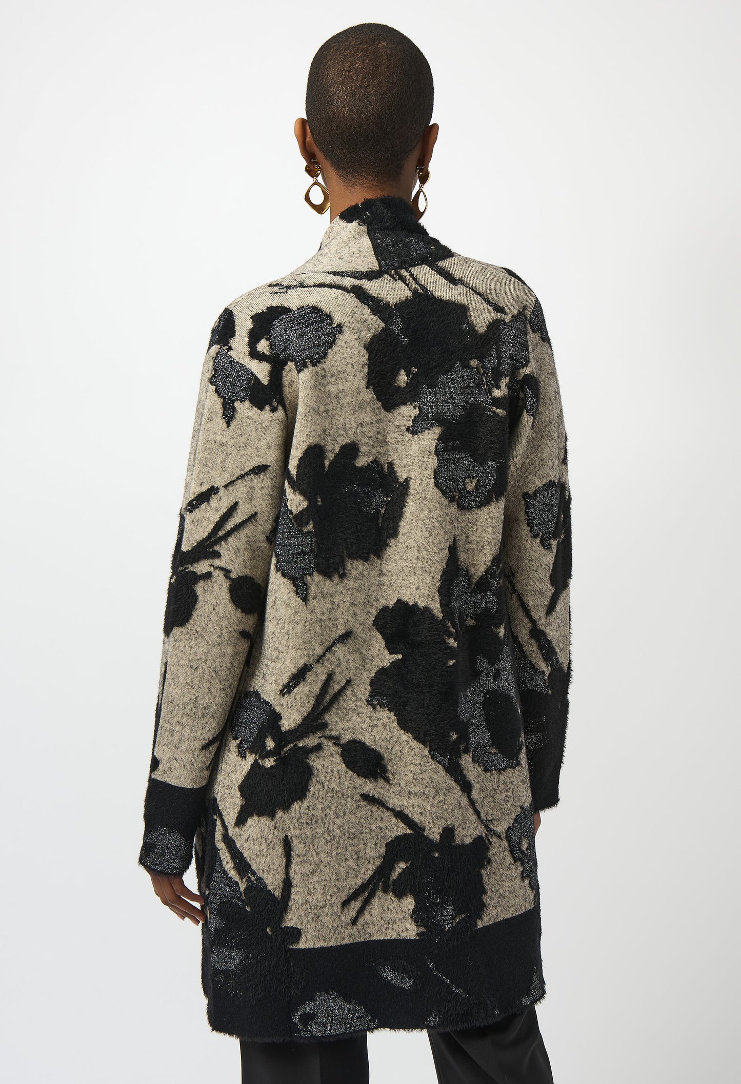 Person wearing a long, patterned coat with black floral designs on a white background