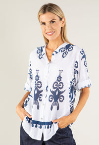 Woman wearing a white blouse with blue patterns on a plain background
