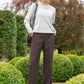 Woman in a light gray sweater and dark brown pants standing in a garden.