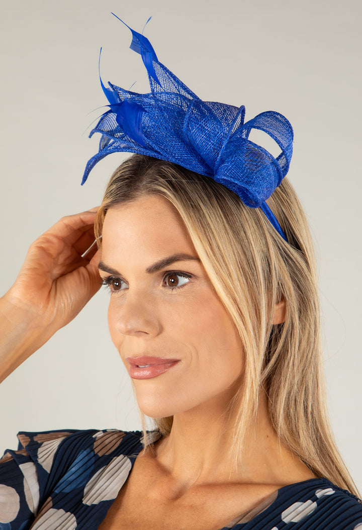 Woman wearing a blue fascinator on a plain background