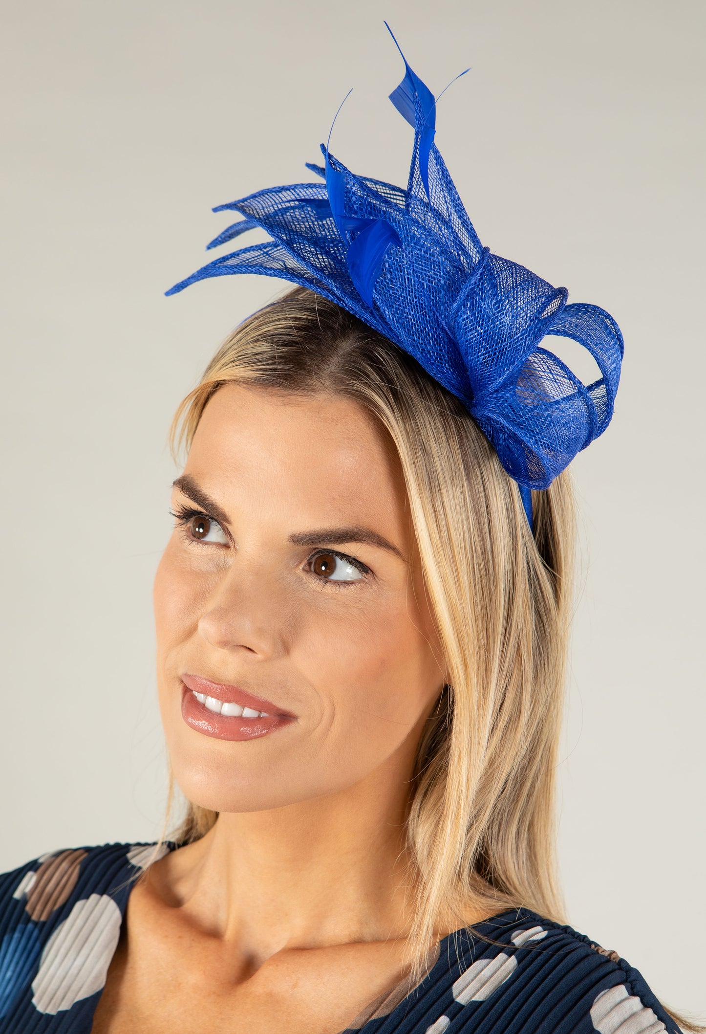 Woman wearing a blue fascinator on a plain background