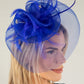 Woman wearing a blue fascinator with feathers on a plain background