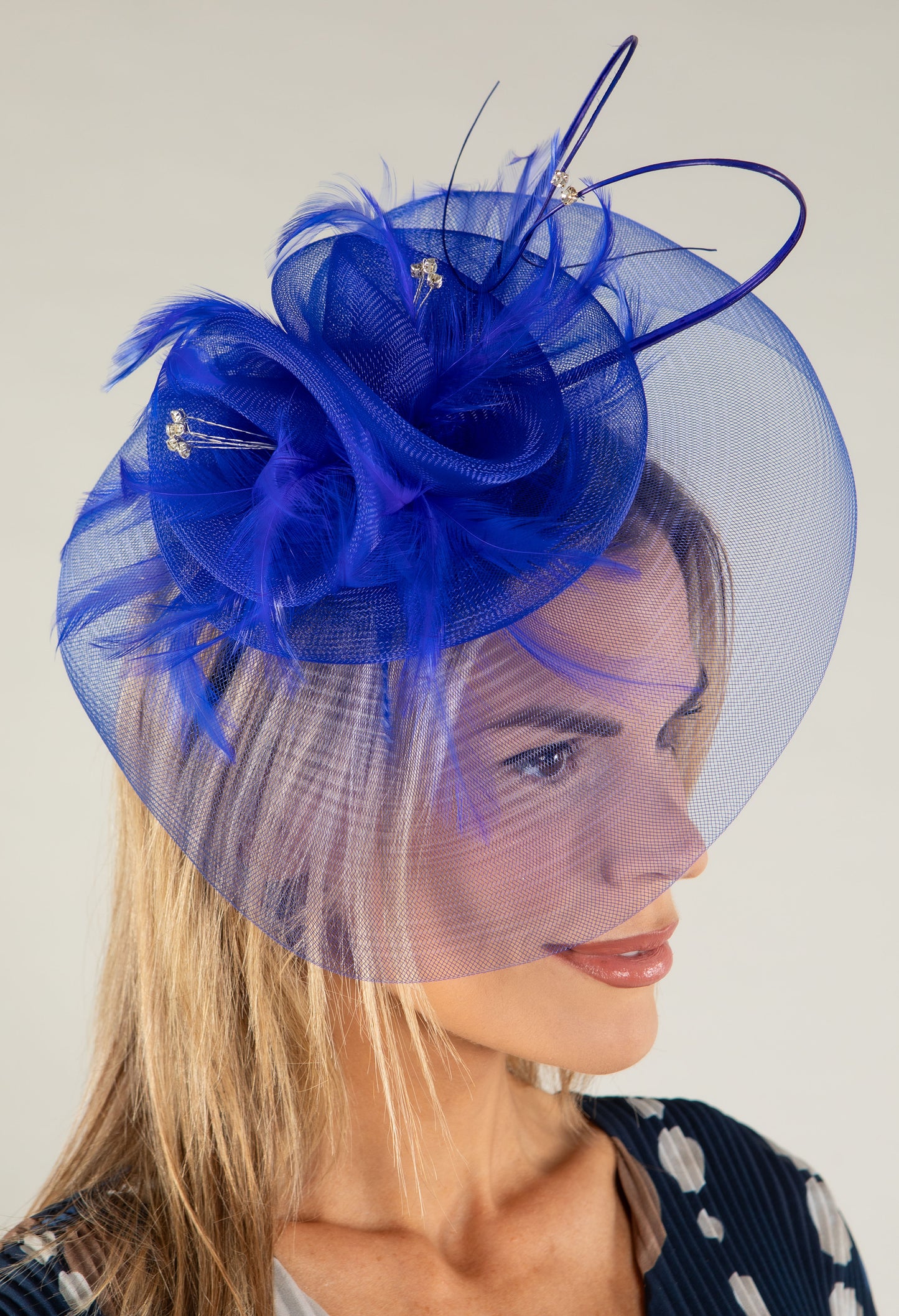 Woman wearing a blue fascinator with feathers on a plain background