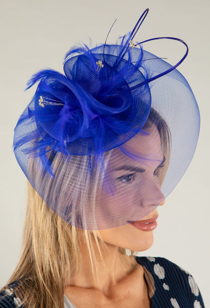 Woman wearing a blue fascinator with feathers on a plain background