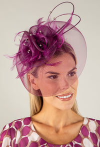 Woman wearing a decorative fascinator with a plain background