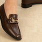 Brown leather shoes with gold buckles on a beige background