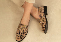 Leopard print loafers worn by a person on a neutral background