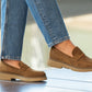 Brown loafers worn with blue jeans on a light background