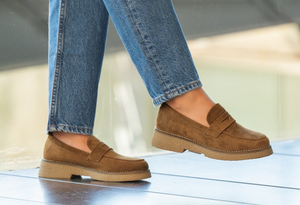 Brown loafers worn with blue jeans on a light background