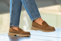 Brown loafers worn with blue jeans on a light background