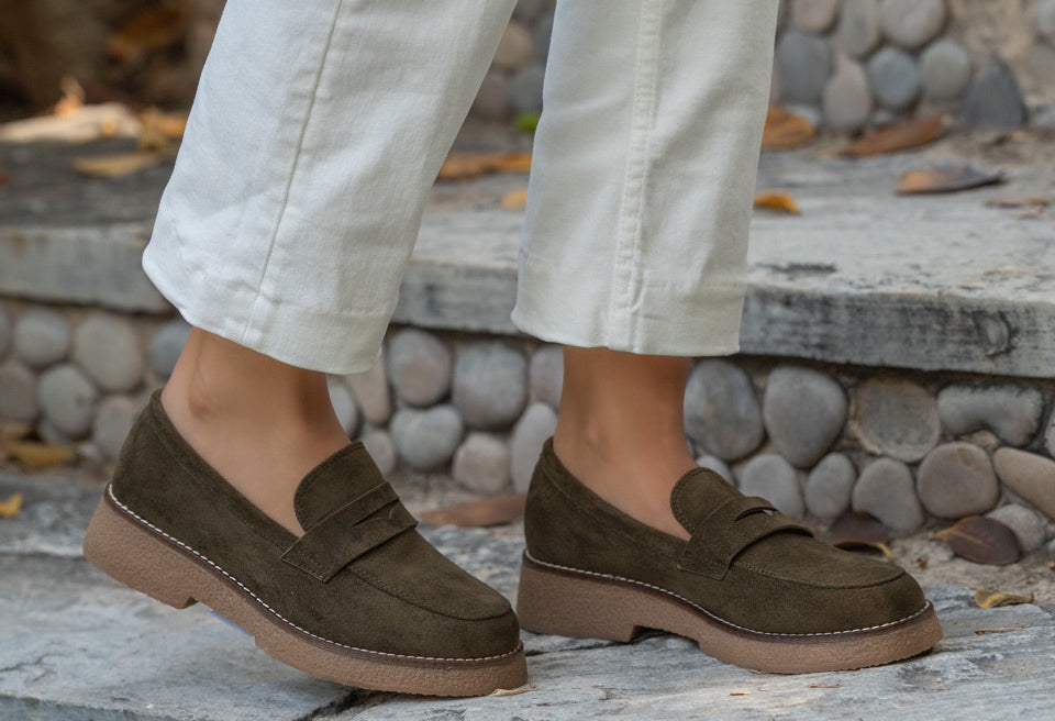 Brown loafers worn with light-colored pants on a stone step.