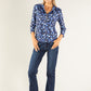 Woman wearing a blue patterned blouse and dark jeans on a white background