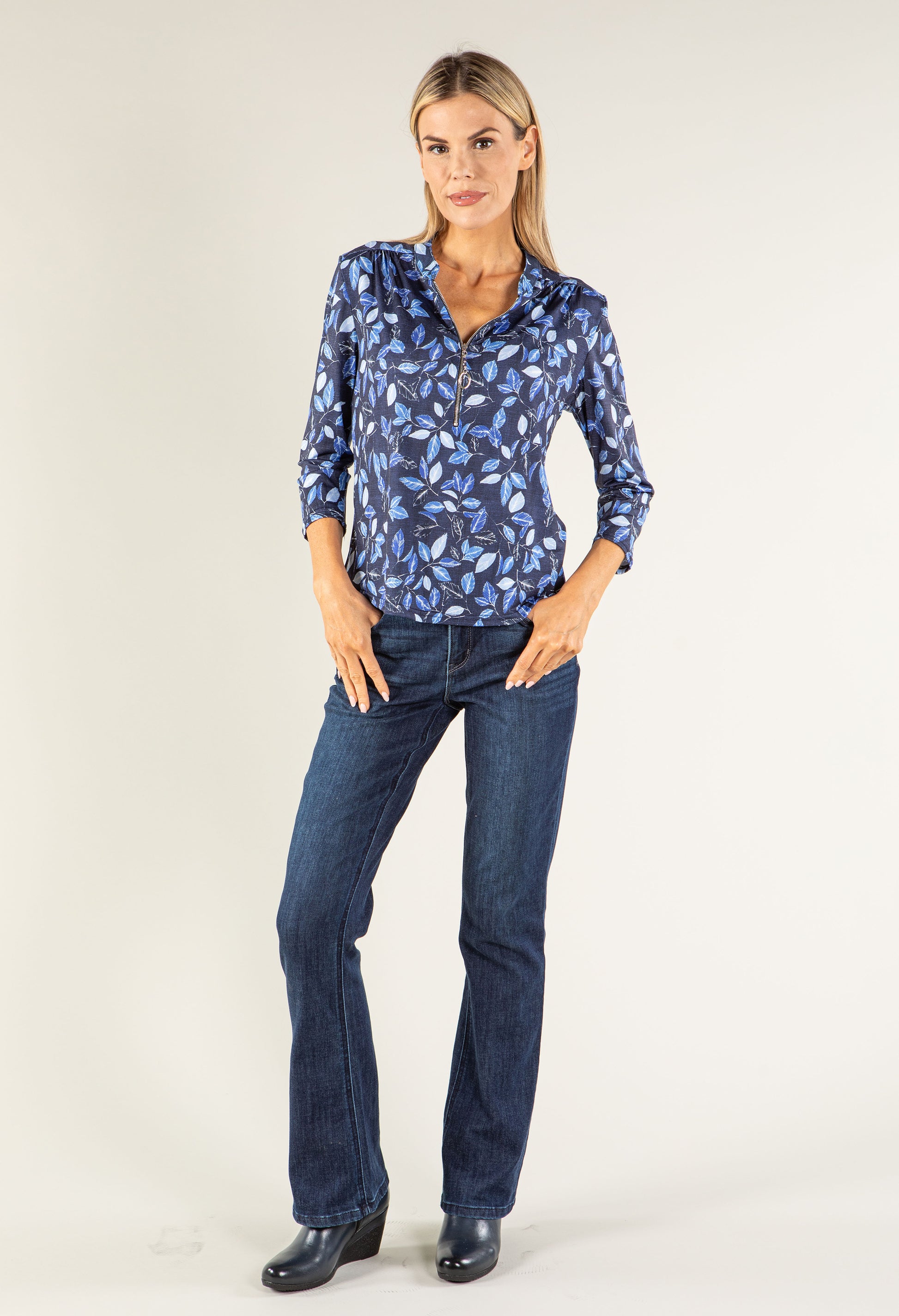 Woman wearing a blue patterned blouse and dark jeans on a white background