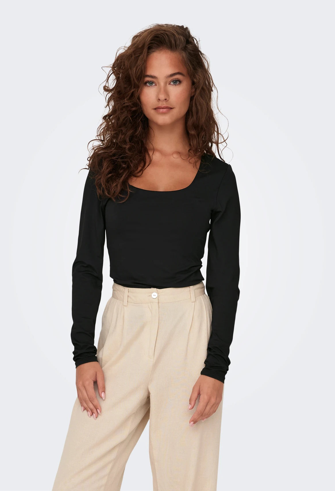 Woman wearing a black long-sleeve top and beige pants on a white background