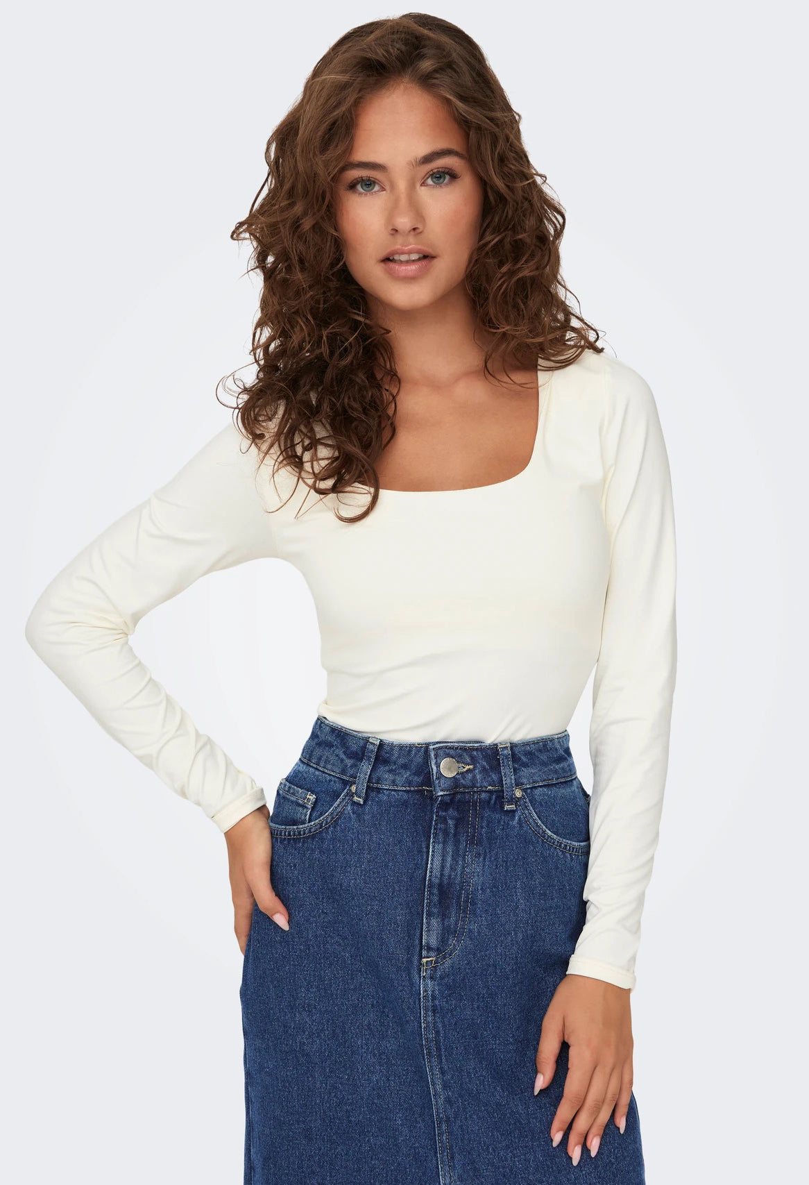 Woman wearing a white long-sleeve top and blue jeans on a plain background