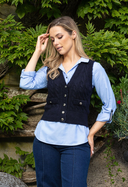 Woman wearing a navy vest over a light blue shirt with a green leafy background