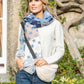 Woman wearing a white sweater and blue jeans with a star-patterned scarf outdoors.