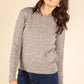 Woman wearing a gray sweater and blue jeans against a beige background